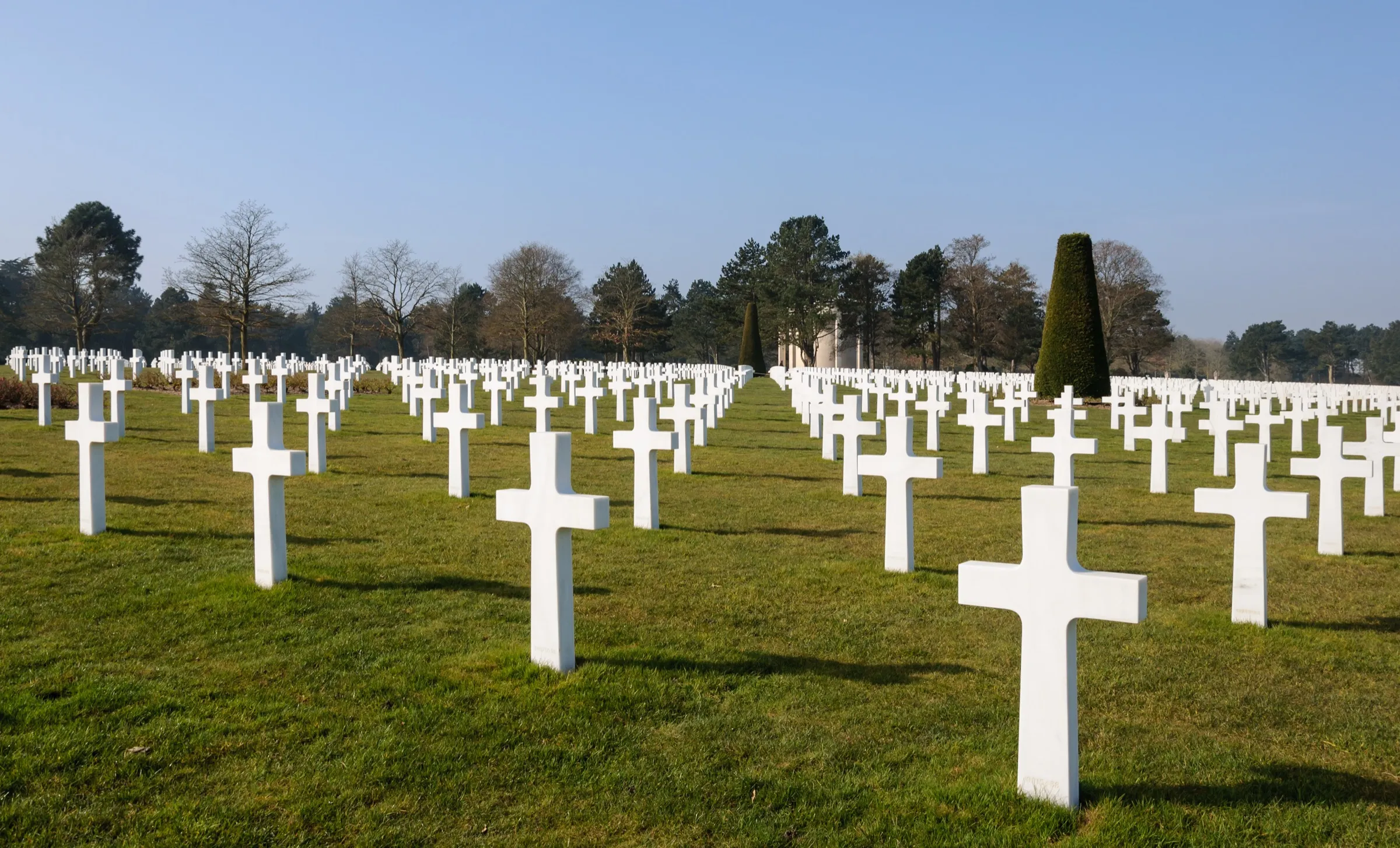 Rangées de croix blanches alignées sur la pelouse du cimetière américain de Colleville-sur-Mer, sous un ciel bleu