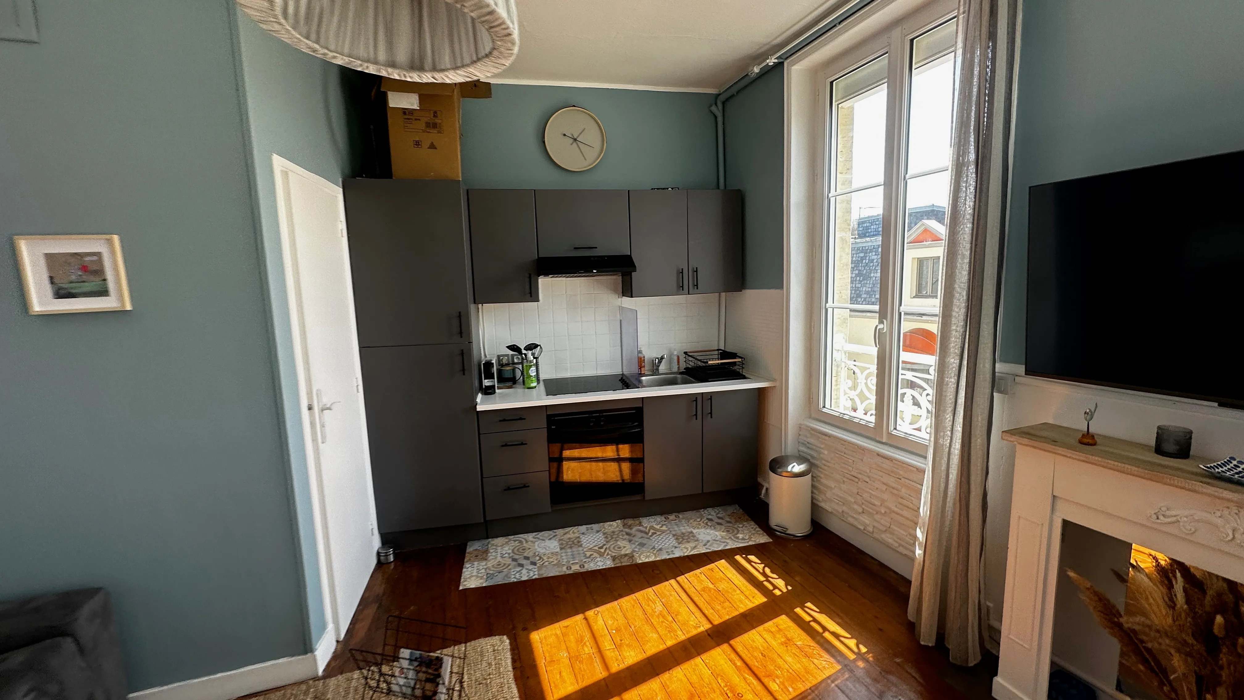 Cuisine du studio dans la lumière du matin, fenêtre ouverte sur les toits du village