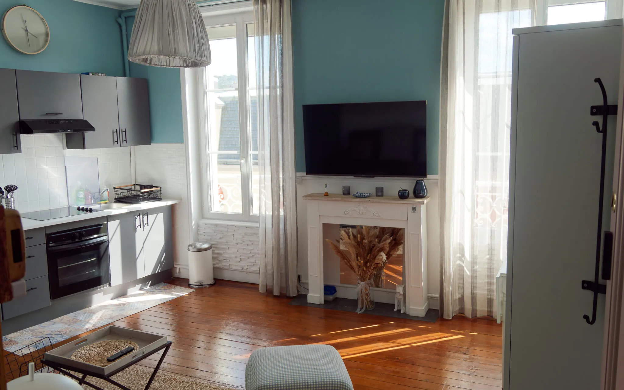 Séjour du studio aux murs bleu canard, parquet ancien et cheminée décorative