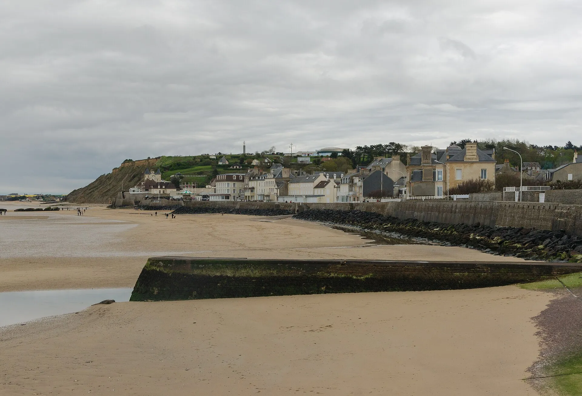 Vue d'ensemble du village d'Arromanches-les-Bains et de sa plage à marée basse, avec les vestiges du port artificiel au large